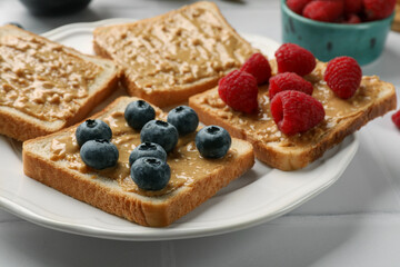 Delicious toasts with peanut butter, raspberries and blueberries on white table, closeup