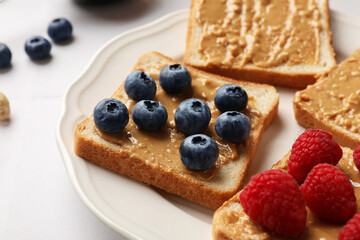 Delicious toasts with peanut butter, raspberries and blueberries on white table, closeup