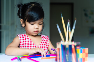 Two years Asian little girl in red and white dress is using colorful pen for painting. Concept of art education and learn through play activity for kid development, talent.