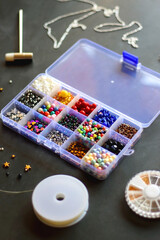 Box with colorful beads, string, wire, chain, scissors, pliers and hammer on dark background. Various jewelry making supplies. Selective focus.