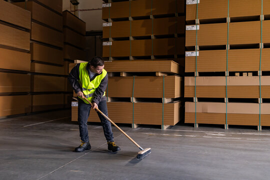 Portrait of young man with Down syndrome sweeping the floor, working in factory, warehouse. Concept of workers with disabilities, support in workplace.