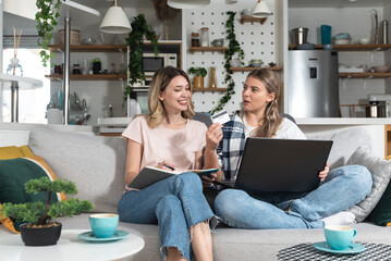 Two young women sitting on the sofa using laptop computer and credit card for online shopping and...