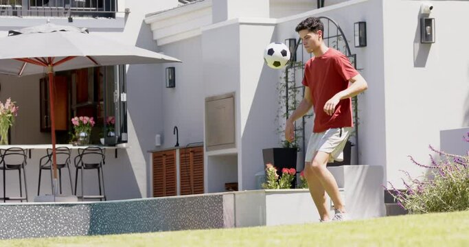 Focused biracial man juggling football with thighs in sunny garden, copy space, slow motion