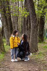 Beautiful young mom walking hand in hand with her young daughter in the park. Mom and daughter walking down an alley holding hands tightly together. Happy Motherhood