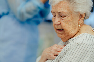Senior woman after stroke, heart attack feeling chest pain. Elderly patient in hospital gown in...