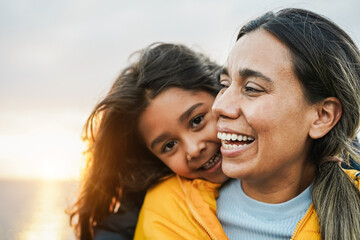 Happy latin mother and daughter having fun together during winter time - Mom day concept - Focus on mum face