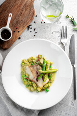 Steamed fillet of white fish with mashed peas and asparagus in a white plate, top view