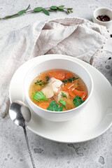 Chicken broth with vegetables and herbs in a white bowl. Transparent soup with homemade chicken.