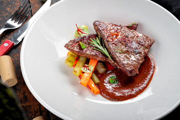 Beef liver stewed with demiglas sauce and served with vegetables on a white plate with rosemary, close-up