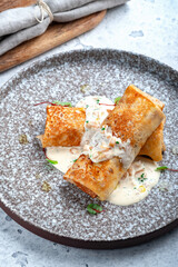 Sweet pancakes with filling rolled into a roll with buttercream and nuts in a gray plate.