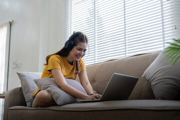 Happy woman wearing headphones watching and listening video on laptop and listening music sitting on a couch at home