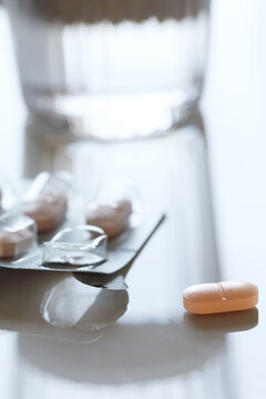 Nahaufnahme von Tablette mit Blisterverpackung vor einem Wasserglas im unscharfen Hintergrund