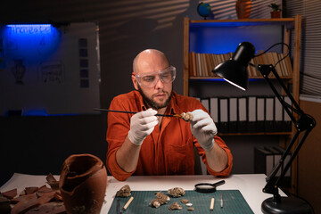 Bearded scientist archaeologist cleaning fossilized ancient coins found at archaeological...