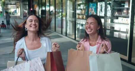 In mall women friends display shopping bags expressing vibrant emotions close-up front view. Women's emotions happiness bonding over shopping Women's emotions sincere joy elegance positivity.