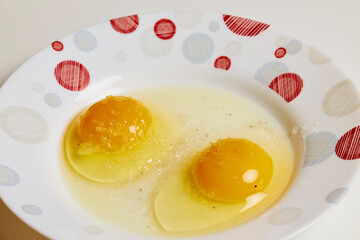 Two raw eggs in a plate with spices on them.
