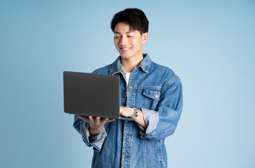Portrait of an Asian guy wearing a jacket and using a laptop posing on a blue background