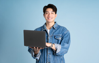 Portrait of an Asian guy wearing a jacket and using a laptop posing on a blue background