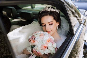 Portrait of an incredibly beautiful bride in the window of an expensive car. The bride with a bouquet of flowers tenderly looks at the flowers.