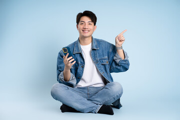Full body image of Asian guy using phone on blue background