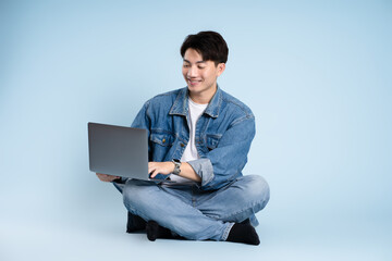 Full body image of Asian guy using laptop on blue background