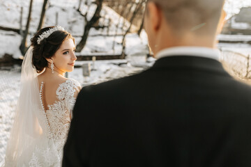 Naklejka premium Winter wedding. A happy couple in wedding clothes are hugging and smiling in a winter park covered with snow on their wedding day. Winter love story of a beautiful couple in snowy winter weather