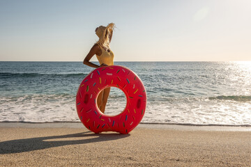 Happy woman with inflatable donut on a tropical beach. Summer vacation concept.