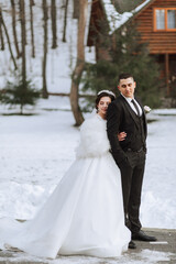 Naklejka premium Winter wedding. Happy couple walking in wedding clothes hugging and smiling in a winter park covered with snow on their wedding day. Winter love story of a beautiful couple in snowy winter weather