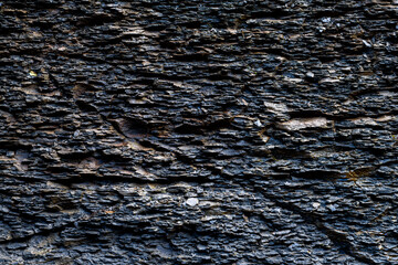 Slate rock background with dark stone layers, cracks caused by erosion. Wet rough surface near a...