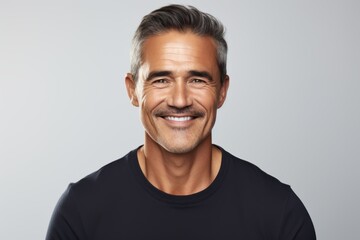 Handsome middle-aged man in black t-shirt smiling at camera while standing against grey background