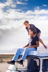 Happy couple enjoy the roof van together having fun in travel holiday alternative vacation - people together in road trip with transport vehicle and love life concept with sky  in background freedom - obrazy, fototapety, plakaty