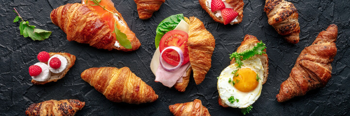Croissant sandwich variety panorama. Various stuffed croissants, overhead flat lay shot on a black...