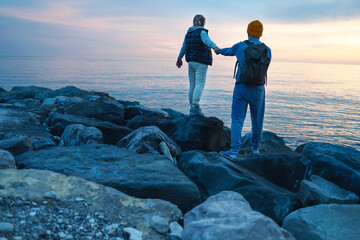 A young couple walks along the seashore at sunset. A man and a woman in casual clothes standing...