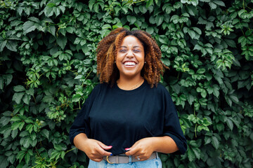 Young positive african woman smiling outside with a ivy plant in the background  at street of city...