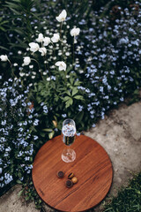 A glass stands on a wooden stand in the midst of a garden lawn and flowerbeds