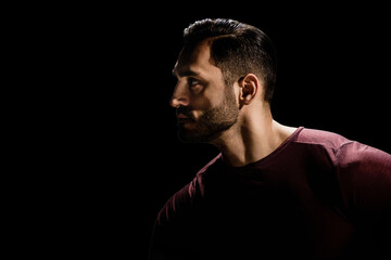 Low key portrait of young man with beard on dark background, Dramatic ambiance: Young man's...