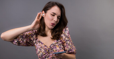 Dancing emotional young woman in stylish clothes listens to music and dances on a gray background