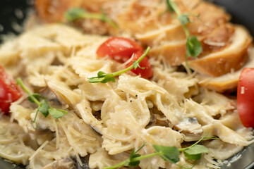Close-up of bowtie pasta with cream sauce, mushrooms, chicken fillet and fresh tomatoes