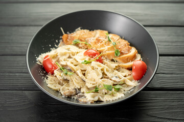 Mushroom pasta farfalle with creamy sauce and tomatoes, on a wooden background. Italian dinner