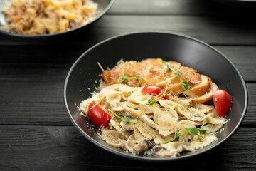Farfalle with mushrooms, chicken fillet and parmesan in cream sauce in a black plate on the wooden table. Traditional Italian pasta on a dark culinary background.