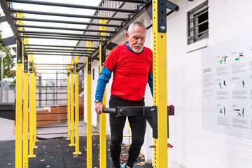 An older athlete takes a break from his pull-up routine at an outdoor fitness park.