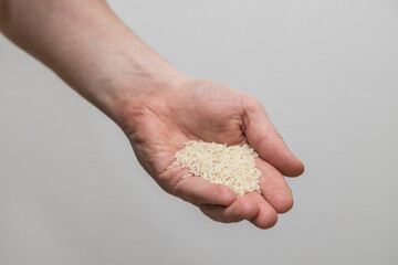 A Caucasian man holds raw long-grain rice in a hand.