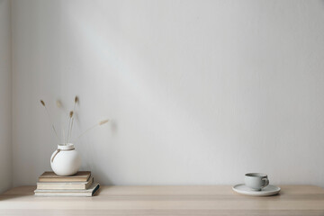 Modern interior. White vase with dray bunny tail grass. Cup of coffee and old books on wooden...