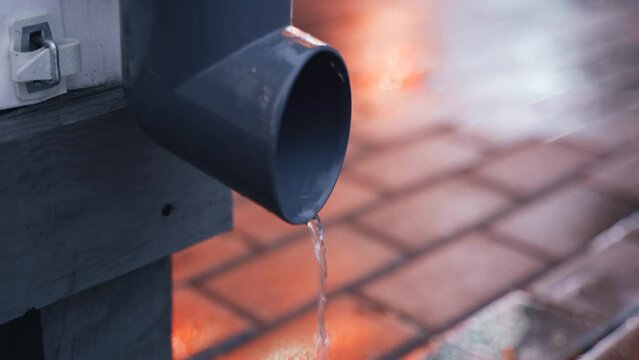 Water flows down a drainpipe onto the sidewalk. Close-up