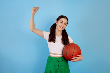 Young brunette teenage girl with basket ball and ponytails on blue background.