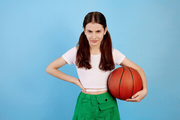 Young brunette teenage girl with basket ball and ponytails on blue background.