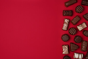 Flat lay of assortment of sweet delicious chocolate candies on a red background. Top view, space for text.