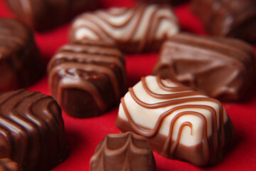 Different chocolate candies on a red background. Assorted sweets on the table. Dark and milk chocolates. Chocolate dessert. Side view. Banner.