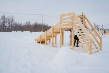 A wooden slide without people stands on a snow field, a children's playground, vacations in the village, a wooden staircase.