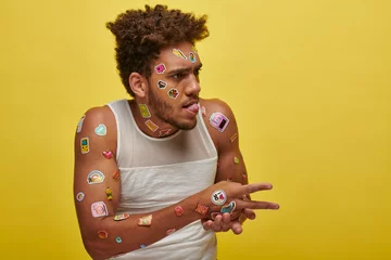 Fotobehang funny african american guy in tank top with stickers on face sticking out tongue on green backdrop © LIGHTFIELD STUDIOS