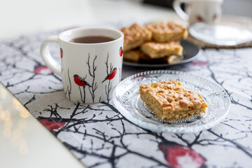 Cups and a napkin with a pattern of bullfinches and Viennese cookies on a plate on the table. Kitchen set. Photo
